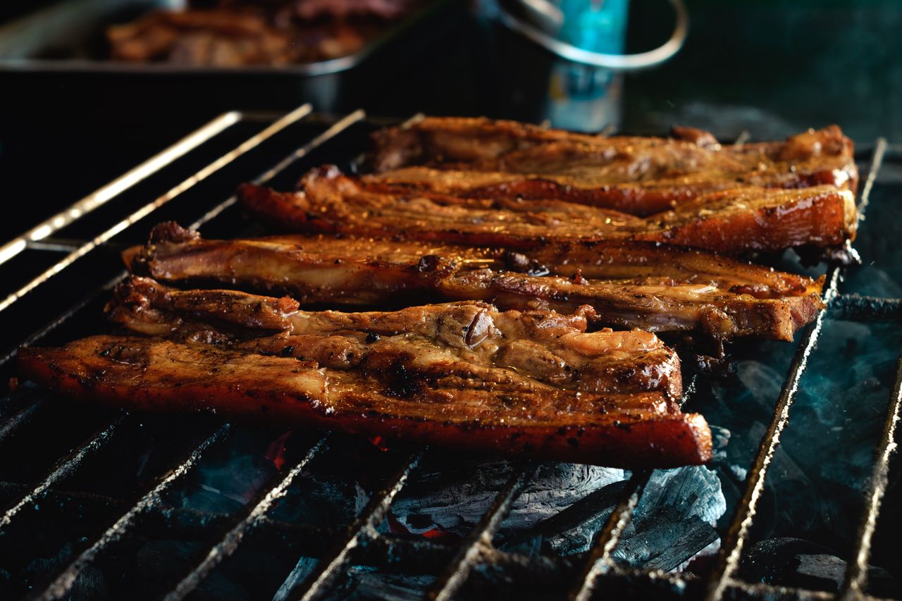 Delicious pork belly slices sizzling on a charcoal grill, perfectly cooked with a smoky finish.